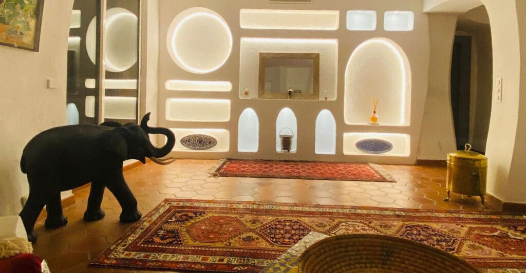 Intérieur de style méditerranéen. Statue d'éléphant, mur blanc avec niches éclairées LED (rond, arches) et tapis orientaux sur carrelage terracotta. Théoule-sur-Mer