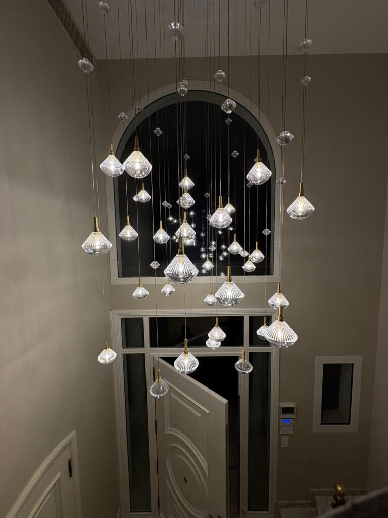 Lustre Design Cascade en Verre pour Entrée Moderne Lustre moderne à multiples suspensions en verre dans une entrée élégante avec une grande fenêtre cintrée de nuit.
